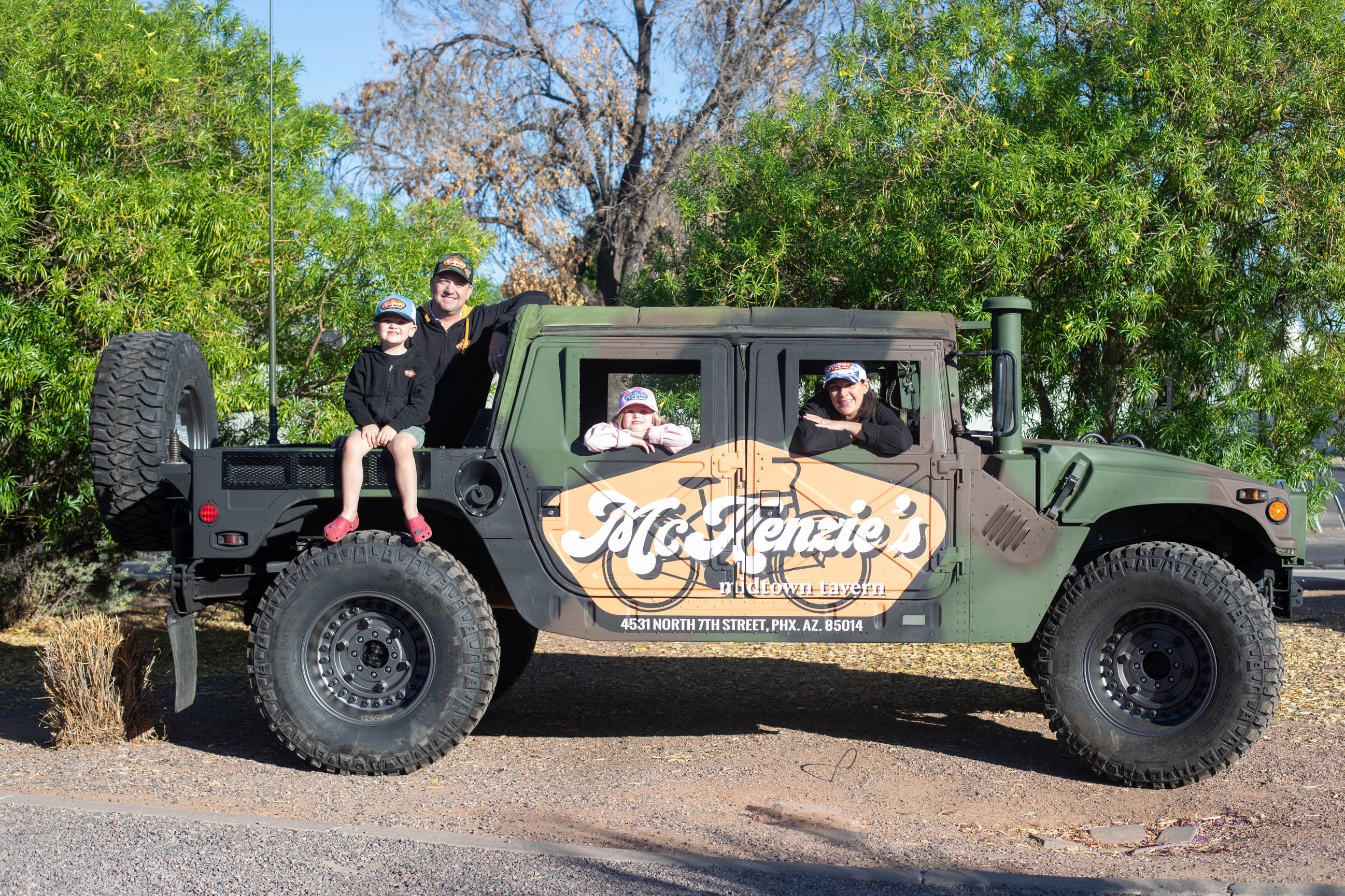 Family posing in a military style vehicle with mckenzies branding on a tree lined street
