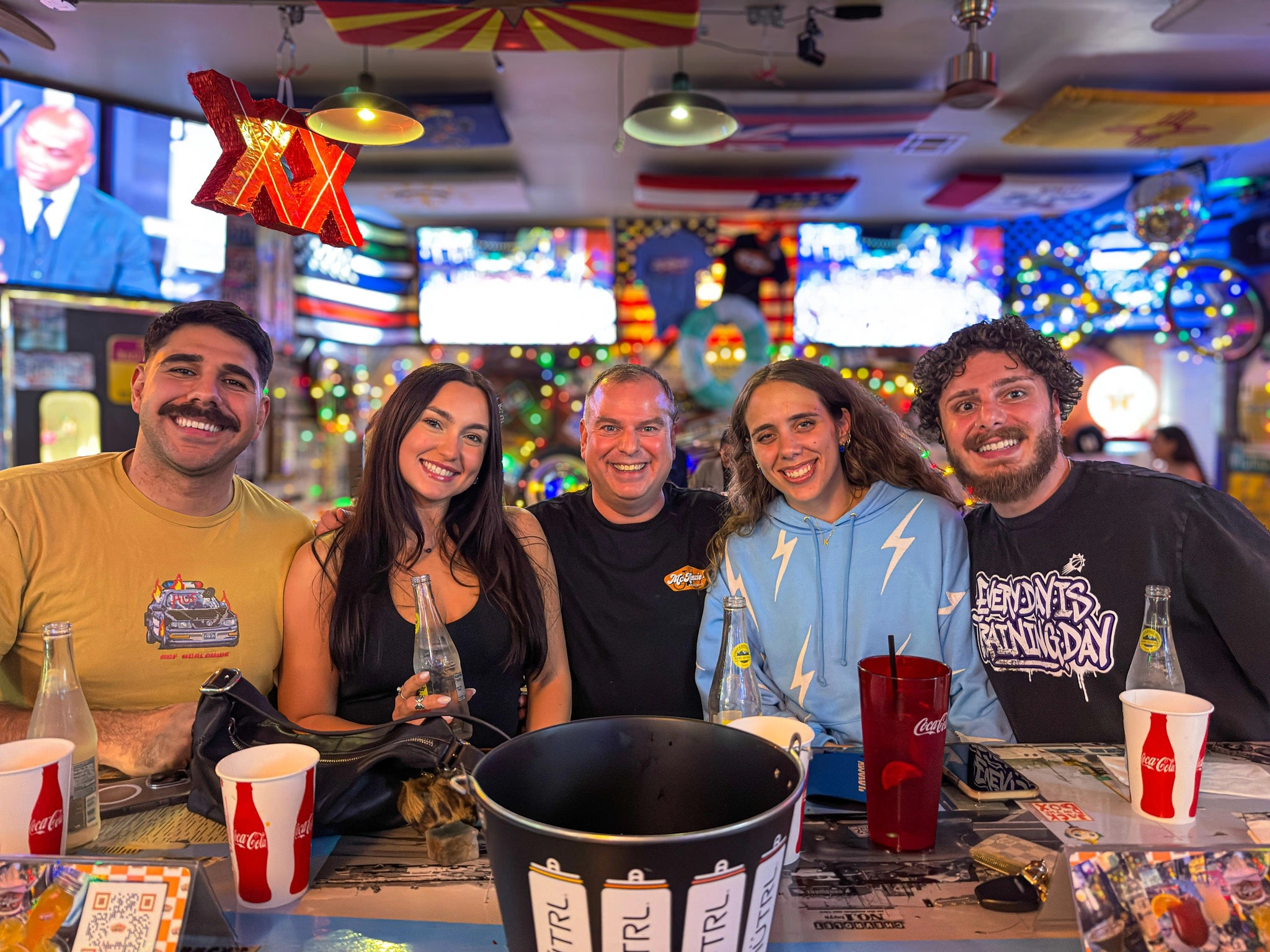 Five friends posing together in McKenzie's bar setting with colorful decor and drinks